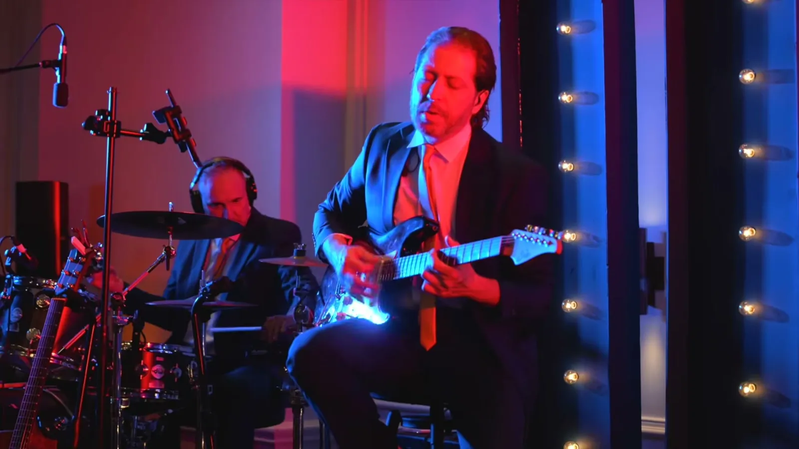 Guitarist and drummer from the gala's live band performing under red and blue stage lighting