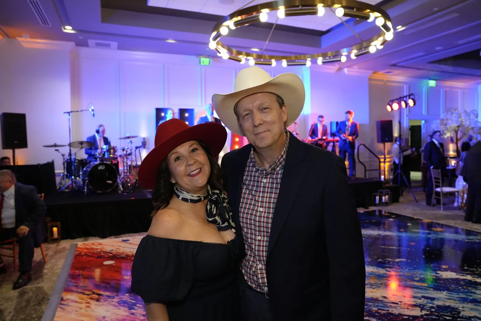 A couple in western hats posing beside the lit dance floor while the live band plays on stage behind them