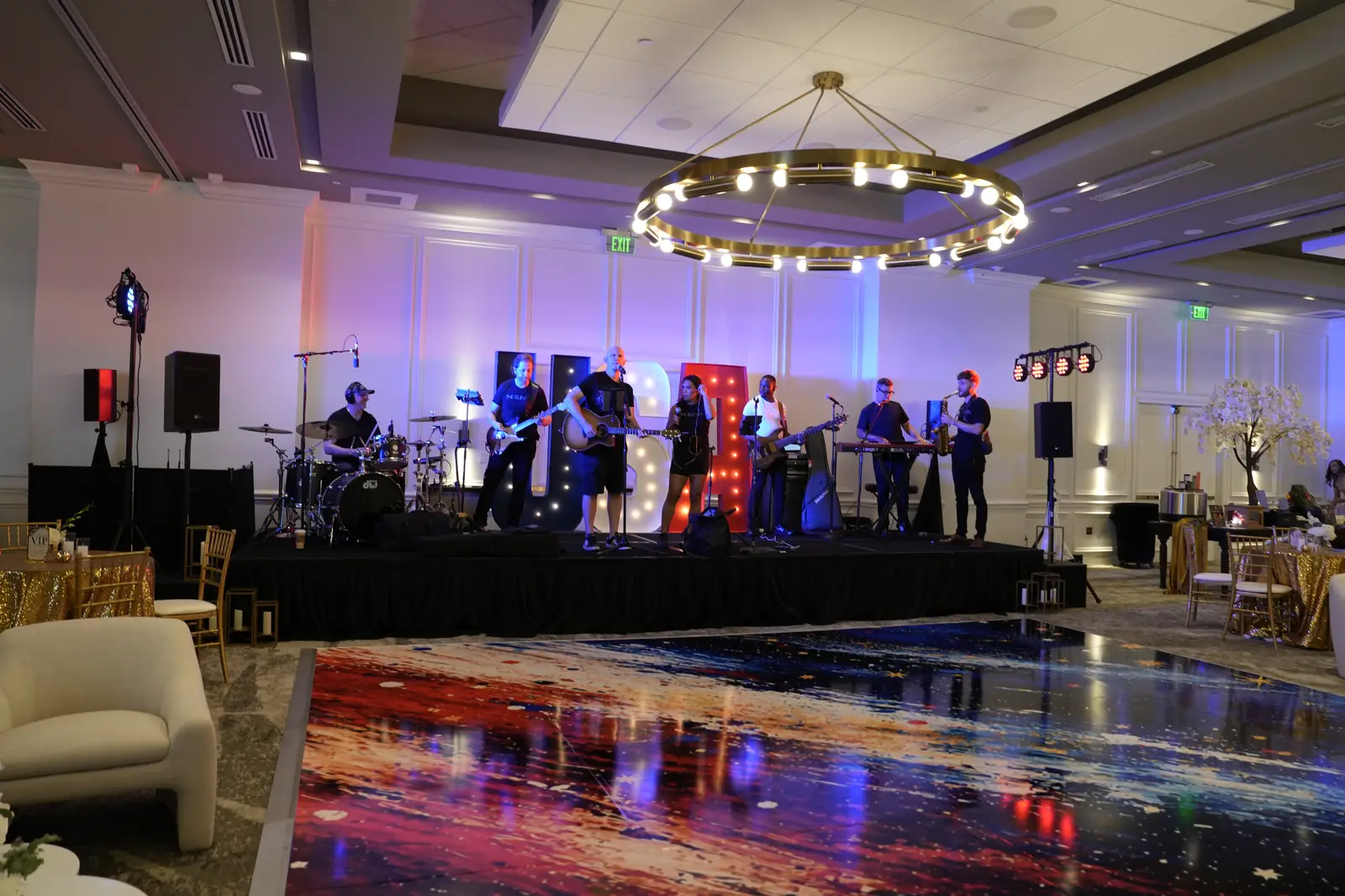 The band on the ballroom stage at PGA National Resort in front of lit USA marquee letters, with the dance floor and lounge chairs still empty