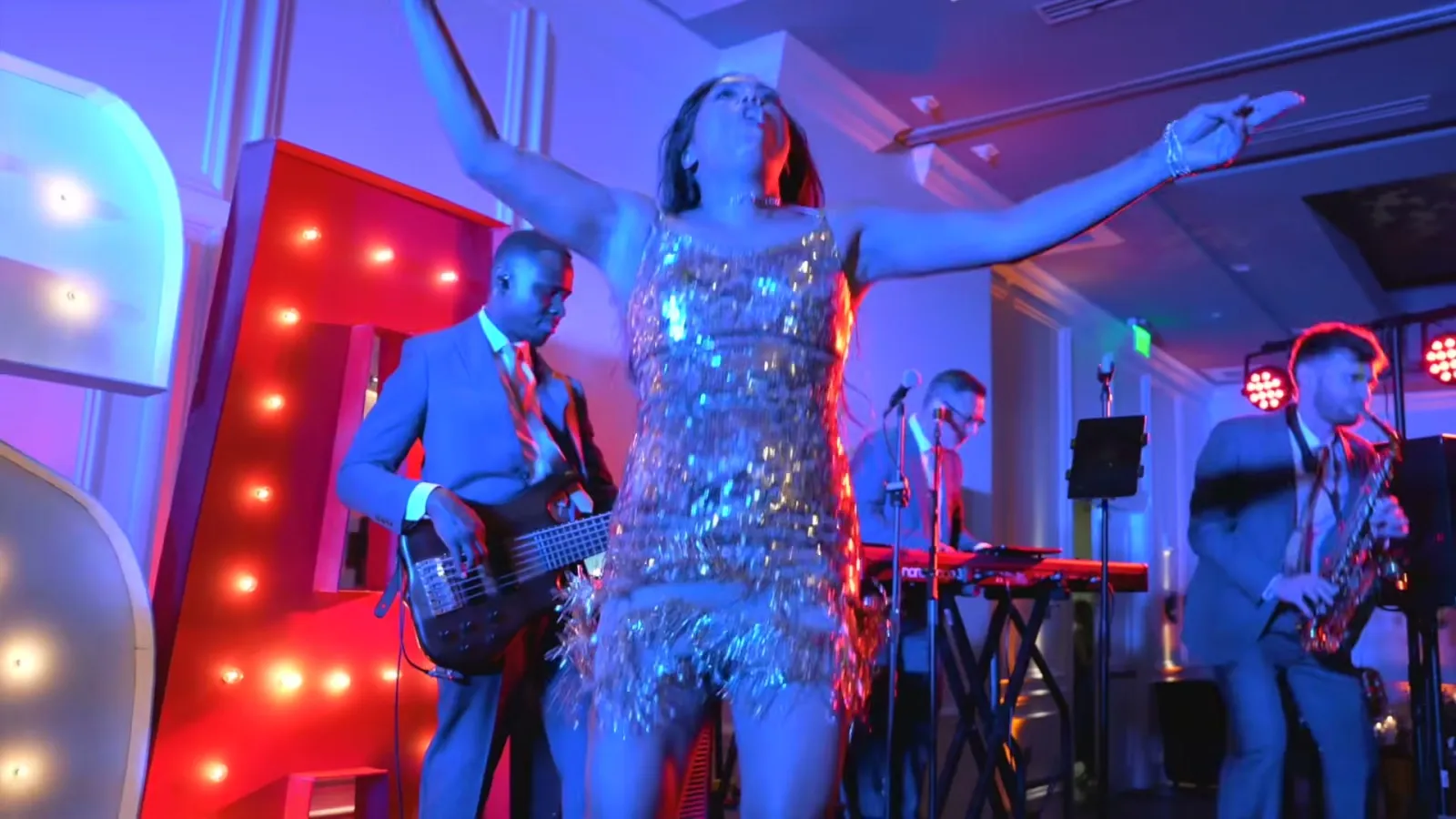 Lead singer in a silver sequined dress performing with the band's bassist, keyboard player and saxophonist at the PGA National gala