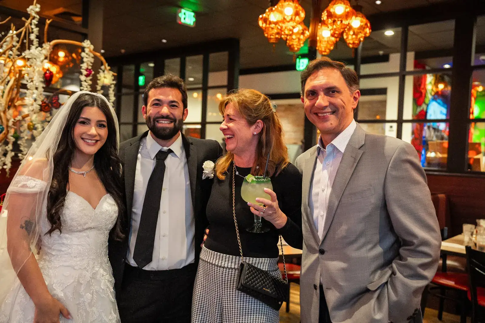 The bride and groom laughing with two guests beneath amber pendant lights at the reception