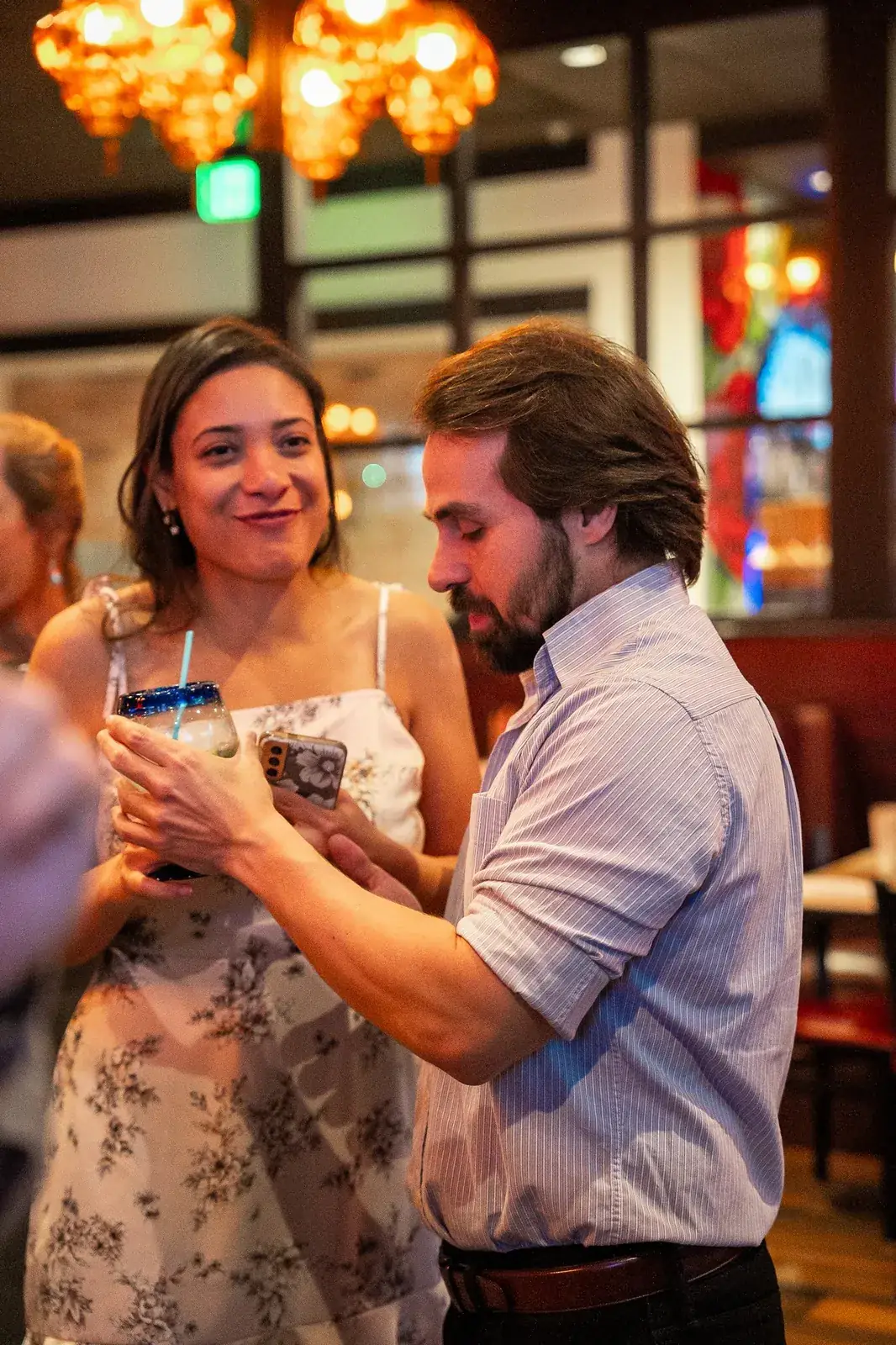 Two wedding guests talking over drinks under warm pendant lights at the reception